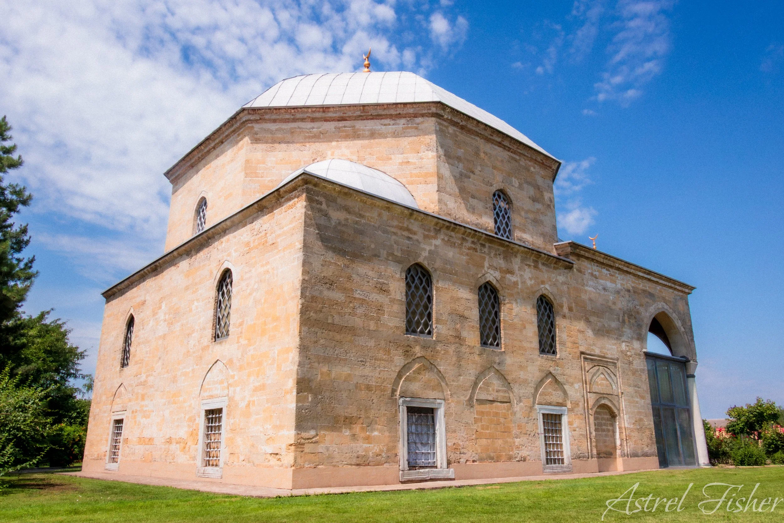 A historic stone church with arched windows and a domed roof topped with a crescent ornament, set against a partly cloudy blue sky.