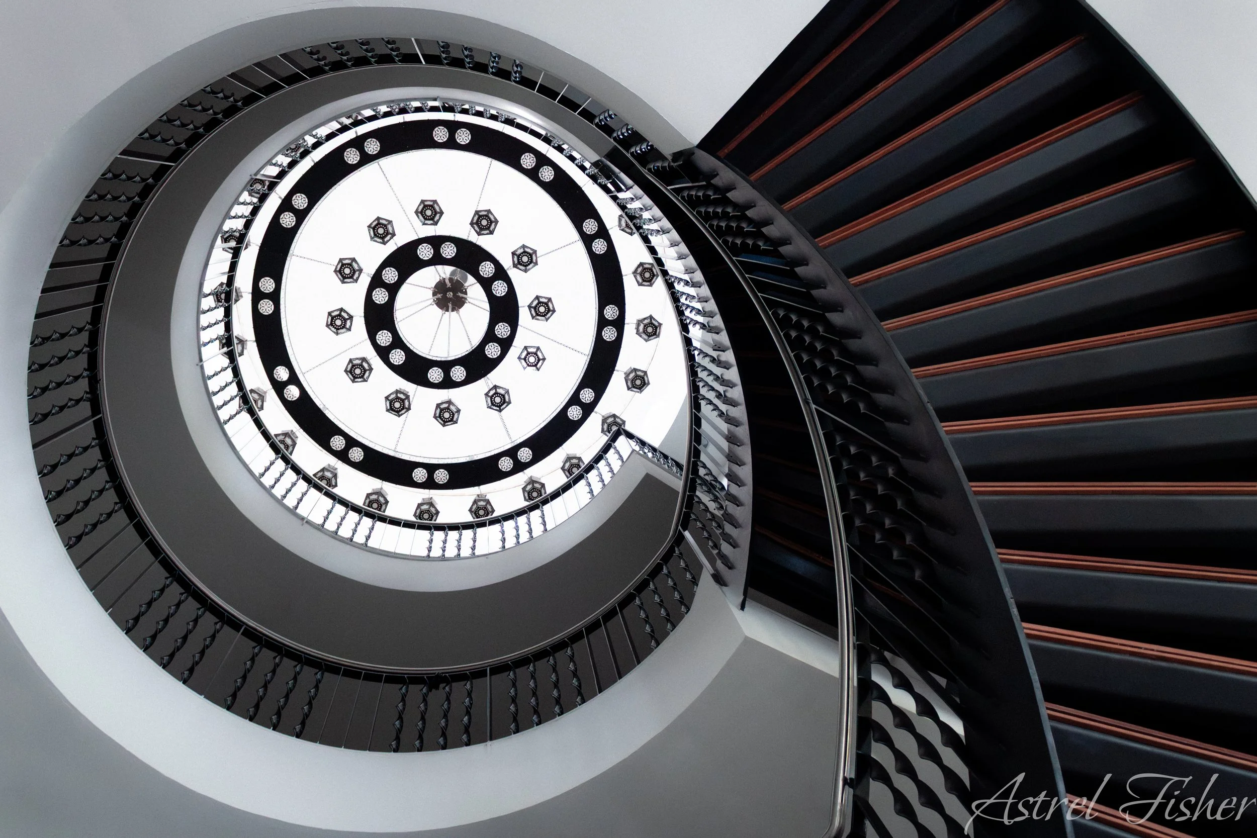 A spiral staircase viewed from below, showing the intricate design of the railing and steps, with a central light fixture at the top.