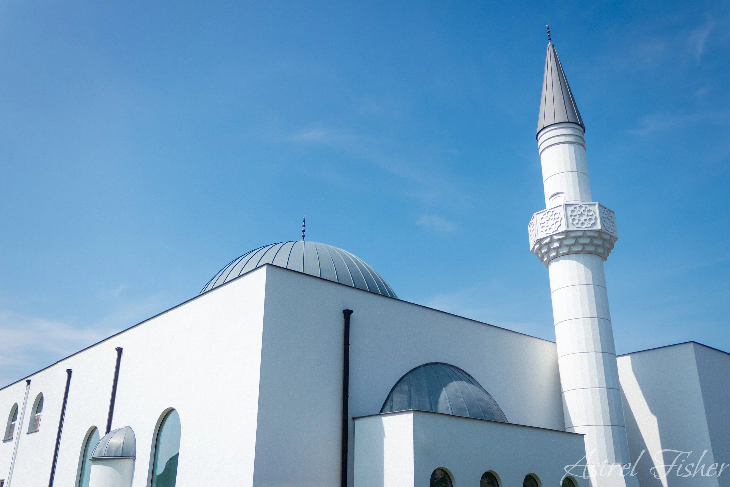 White mosque with a large dome and a tall, narrow minaret against a clear blue sky.