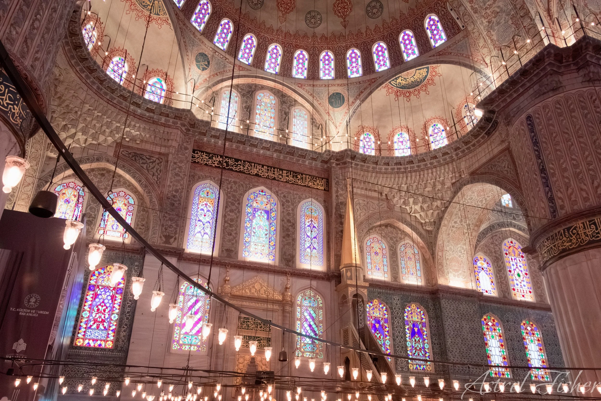 Interior view of a mosque with stained glass windows and ornate decorative patterns on the walls and ceiling.