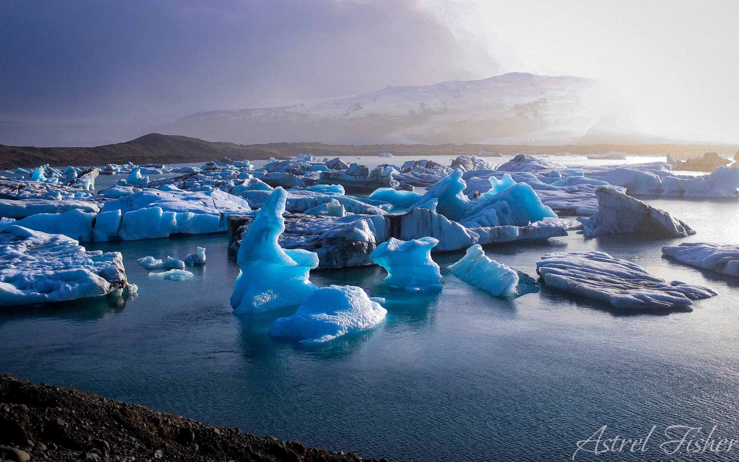 Icebergs floating in a body of water with distant mountains and a sky with soft lighting.