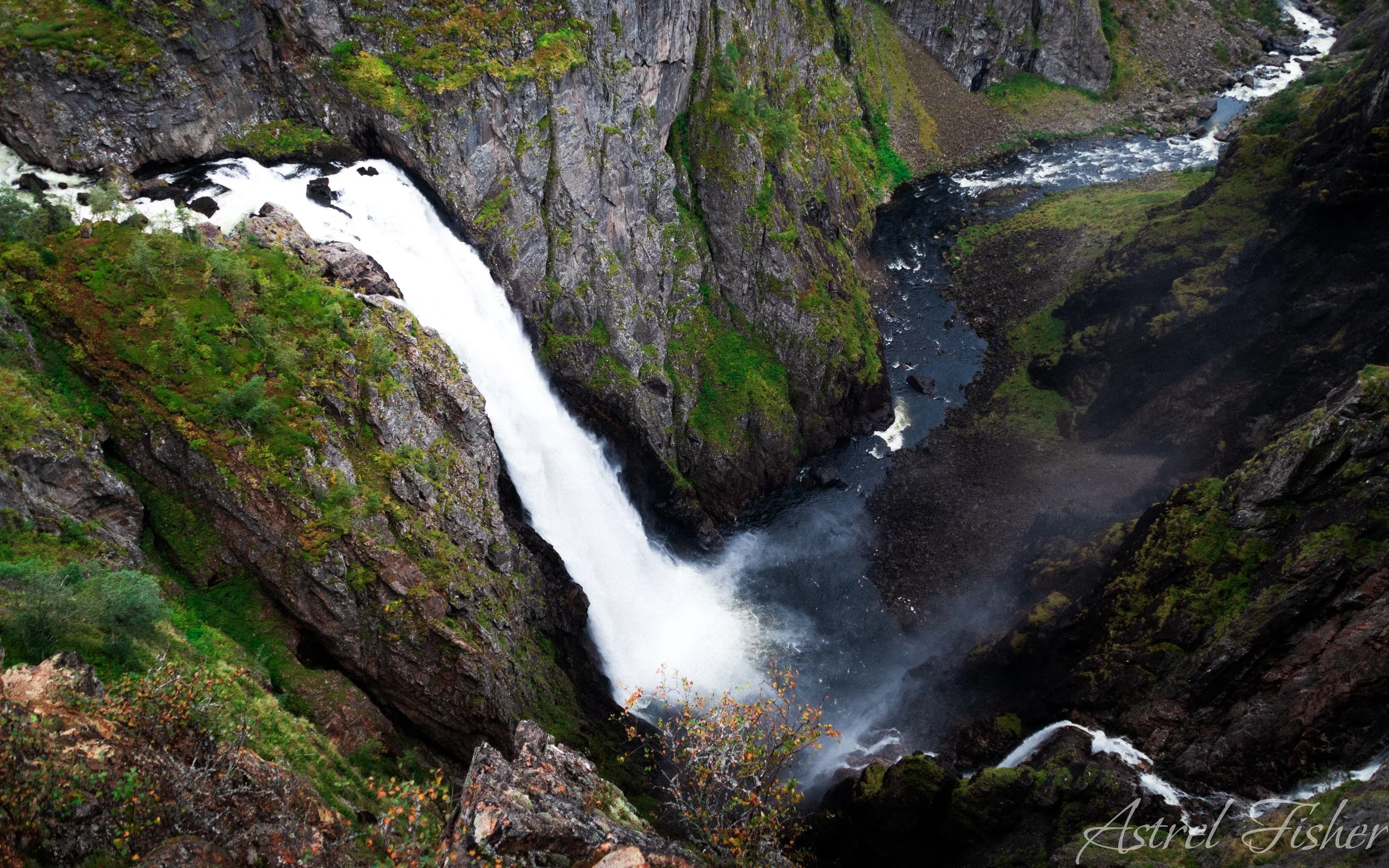 A waterfall flowing down a rocky canyon, surrounded by green moss and vegetation.