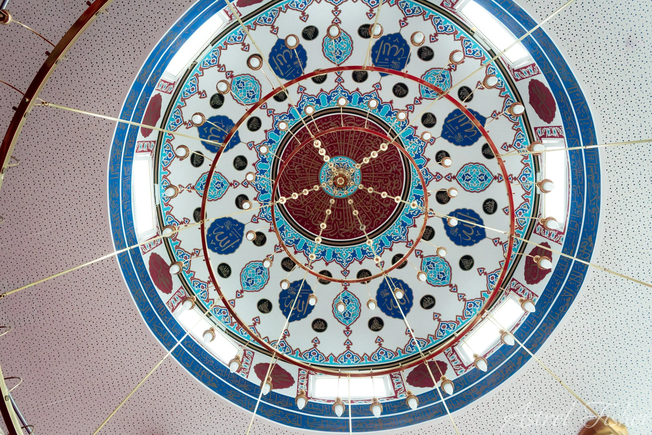 Looking up at an ornate, colorful ceiling with intricate patterns and decorative elements, including circular lights and blue, red, and gold detailing.