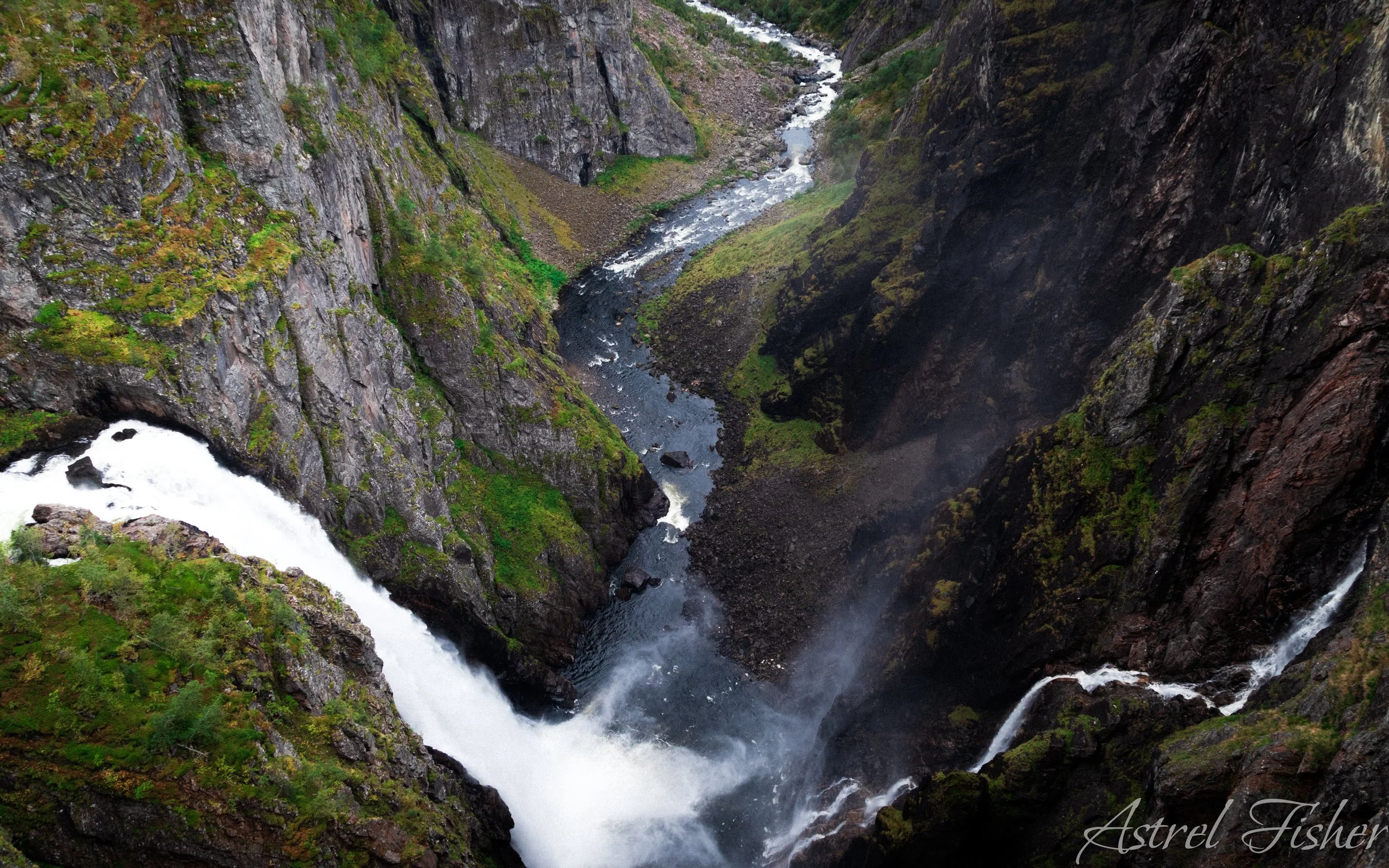 A deep canyon with a rushing river flowing through it, surrounded by steep, rocky cliffs with patches of green vegetation.