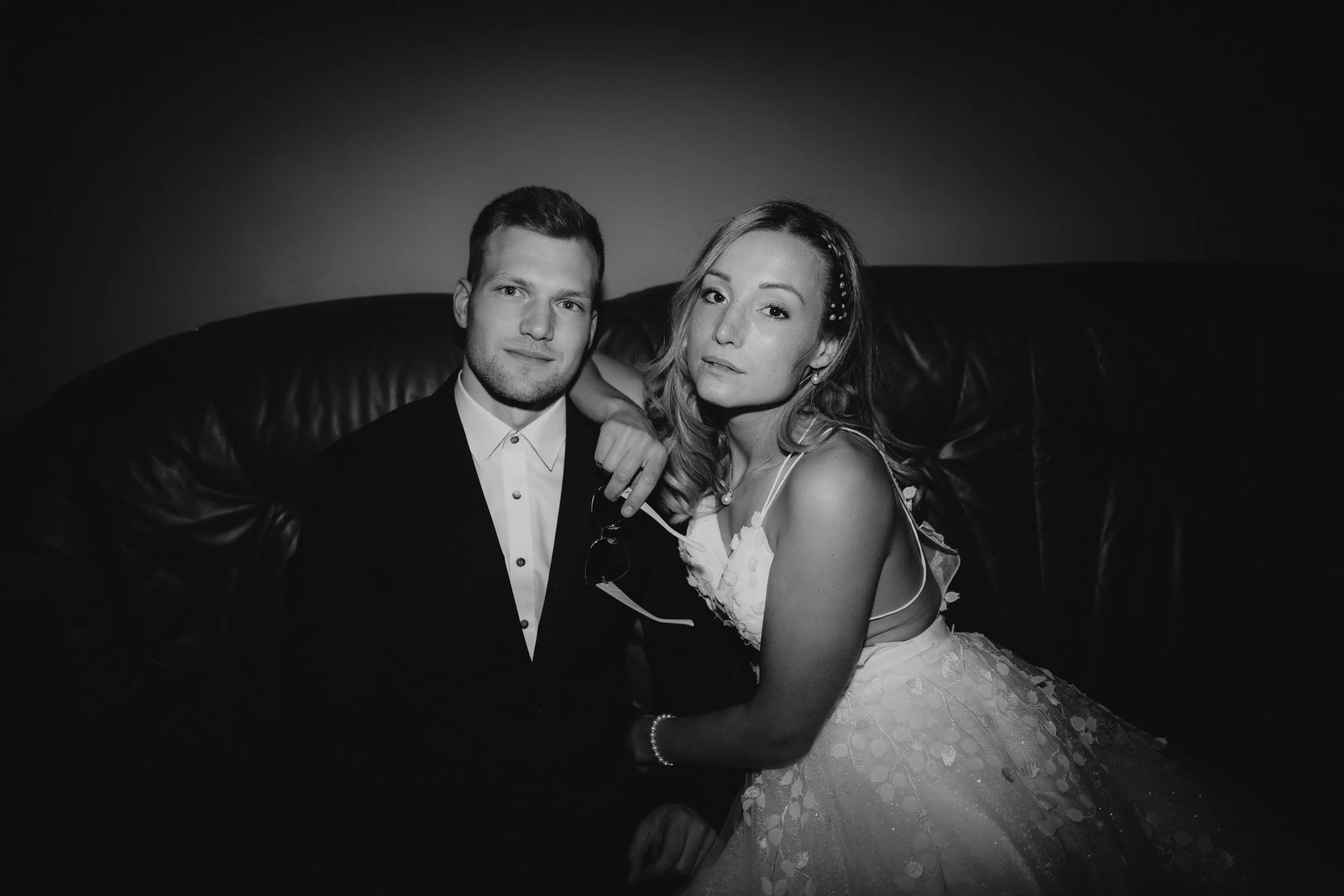 Schwarz-weiß-Foto eines Paares, Mann in Anzug und Frau in Brautkleid, sitzt auf einem Ledersofa.