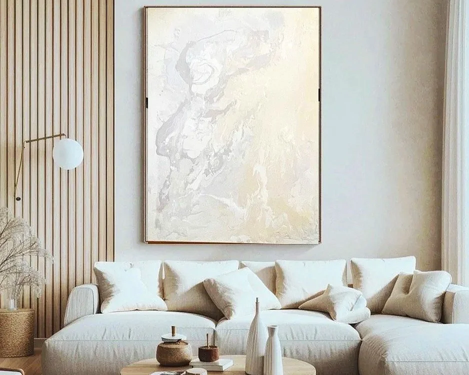 A modern living room with a white sofa, neutral-colored pillows, a wooden coffee table with decorative vases, a wall-mounted lamp, tall curtains, and an abstract painting on the wall.