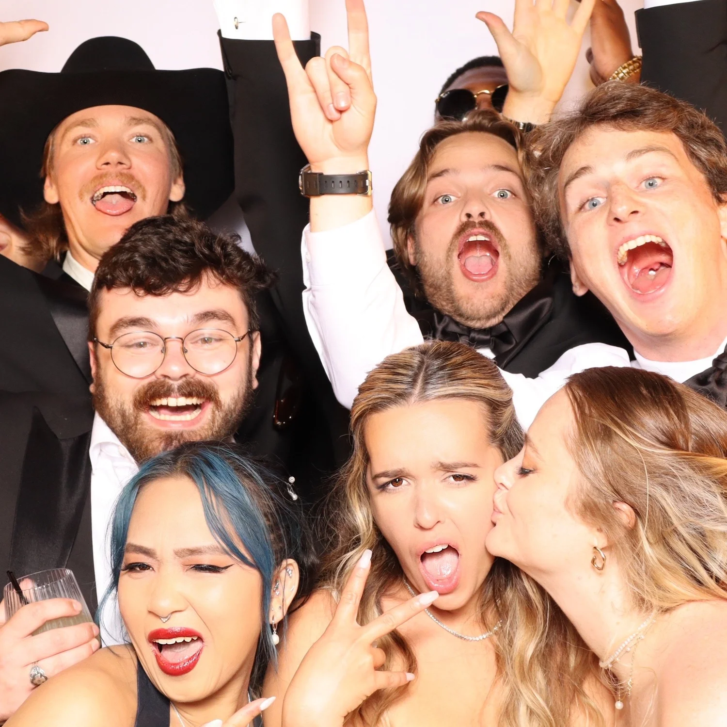 A group of wedding guests crowded together laughing in a studio-lit photo booth portrait at an evening reception at Saddlerock Ranch, Malibu
