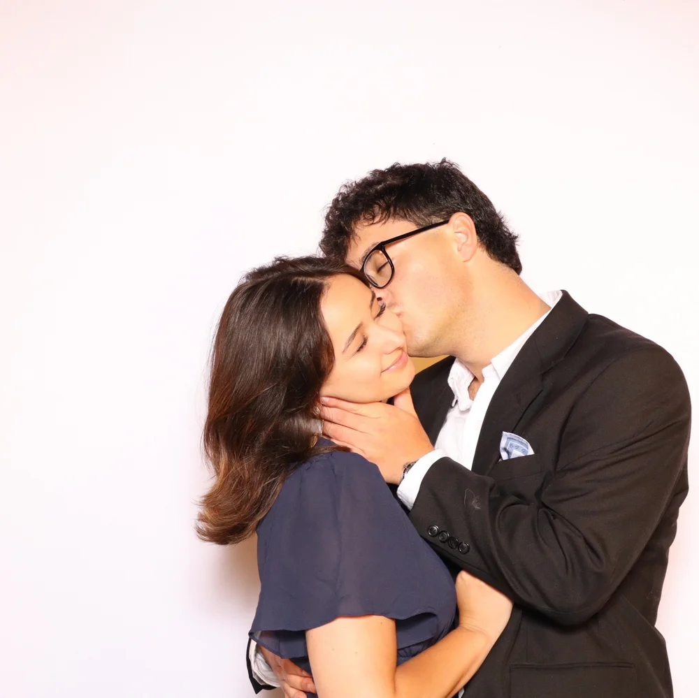 Booth portrait of the same two guests from the setting photo, sharing a kiss, studio-lit outdoors after dark at Saddlerock Ranch
