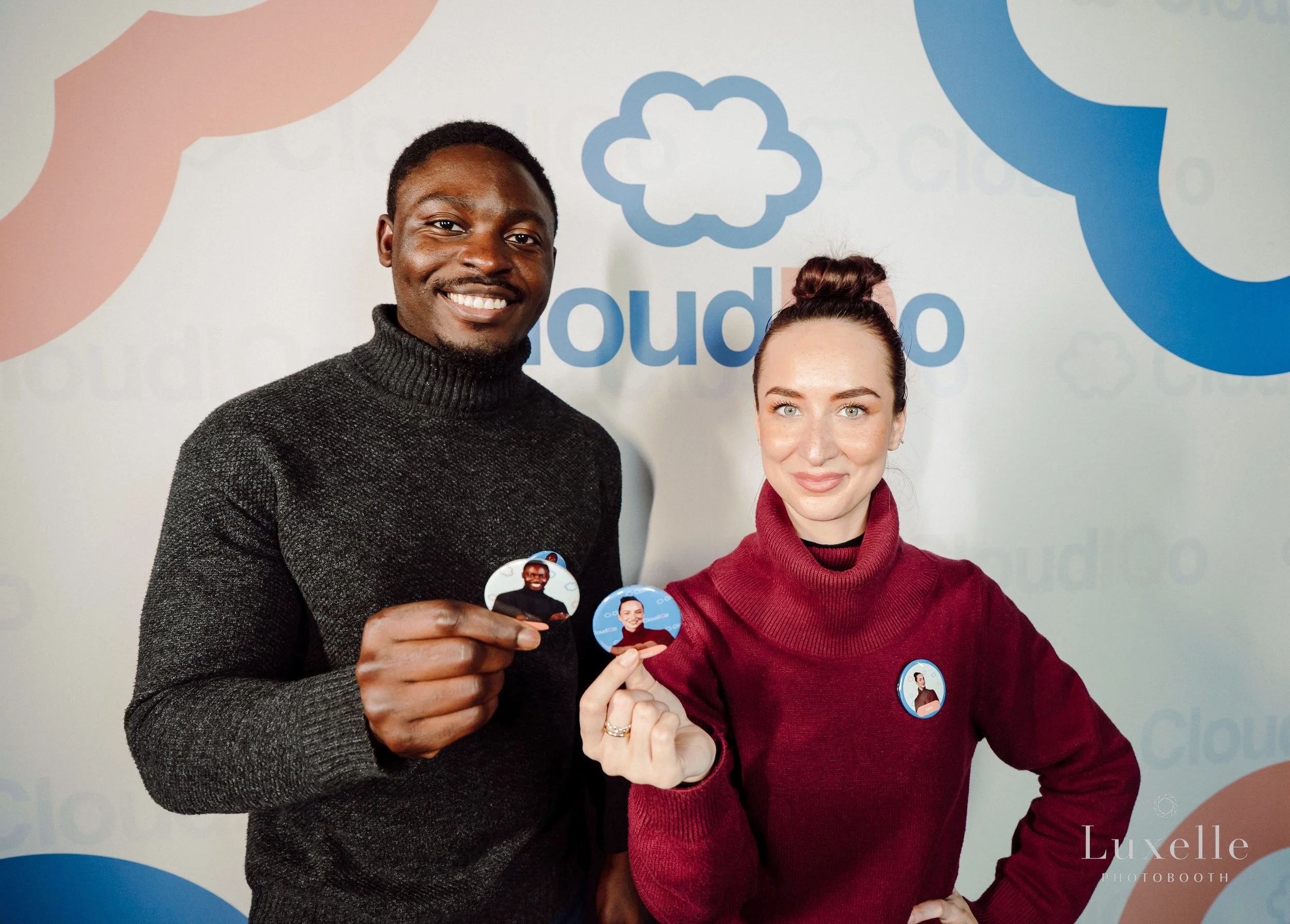Attendees posing at a Luxelle branded corporate photo booth activation with custom step-and-repeat backdrop and photo badges
