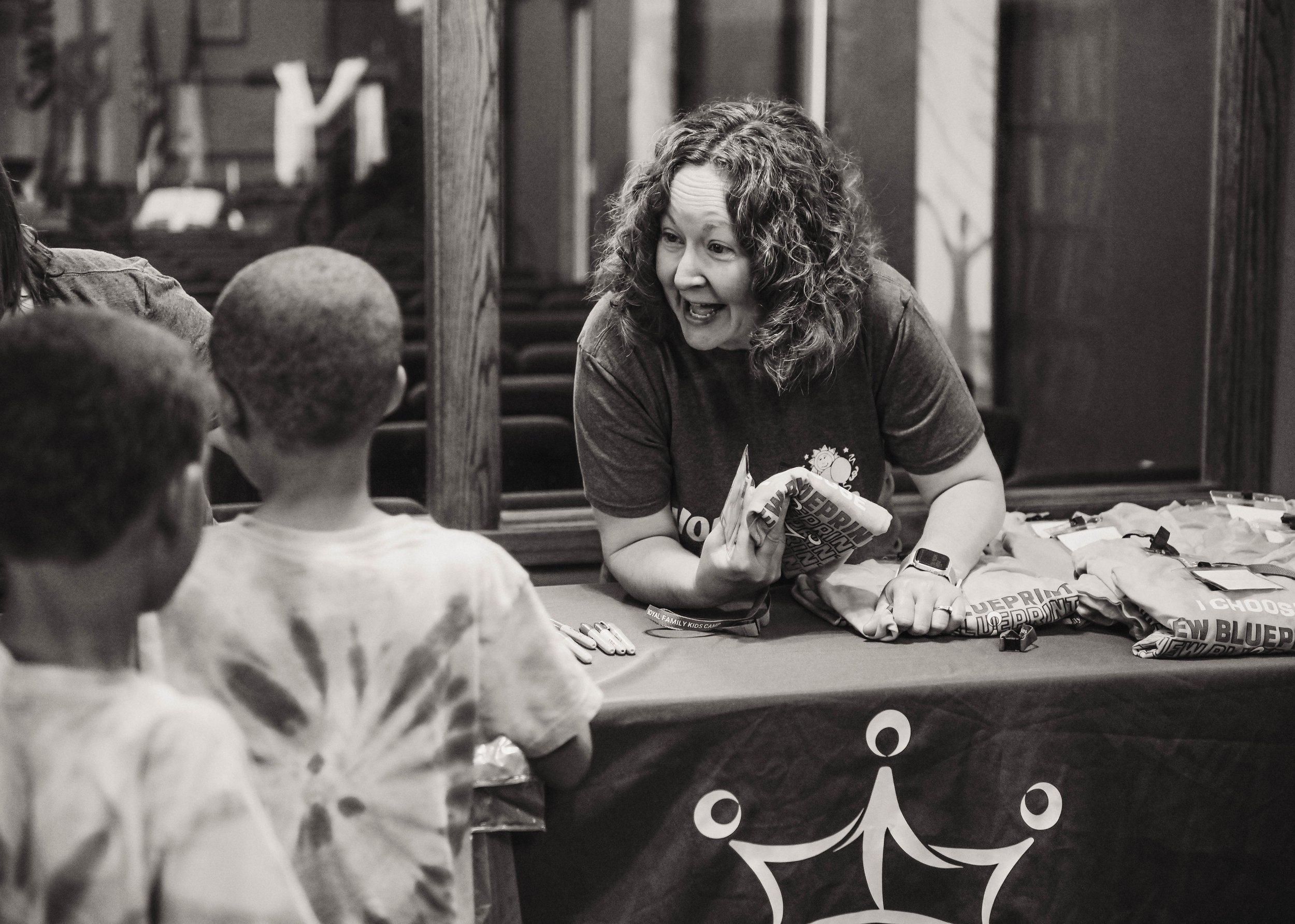 An adult woman working at a registration table smiling and welcoming a camper
