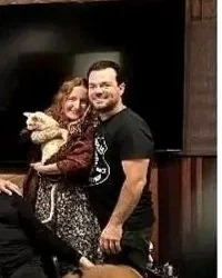 A smiling woman hugging a smiling man inside a dimly lit room with wooden walls.