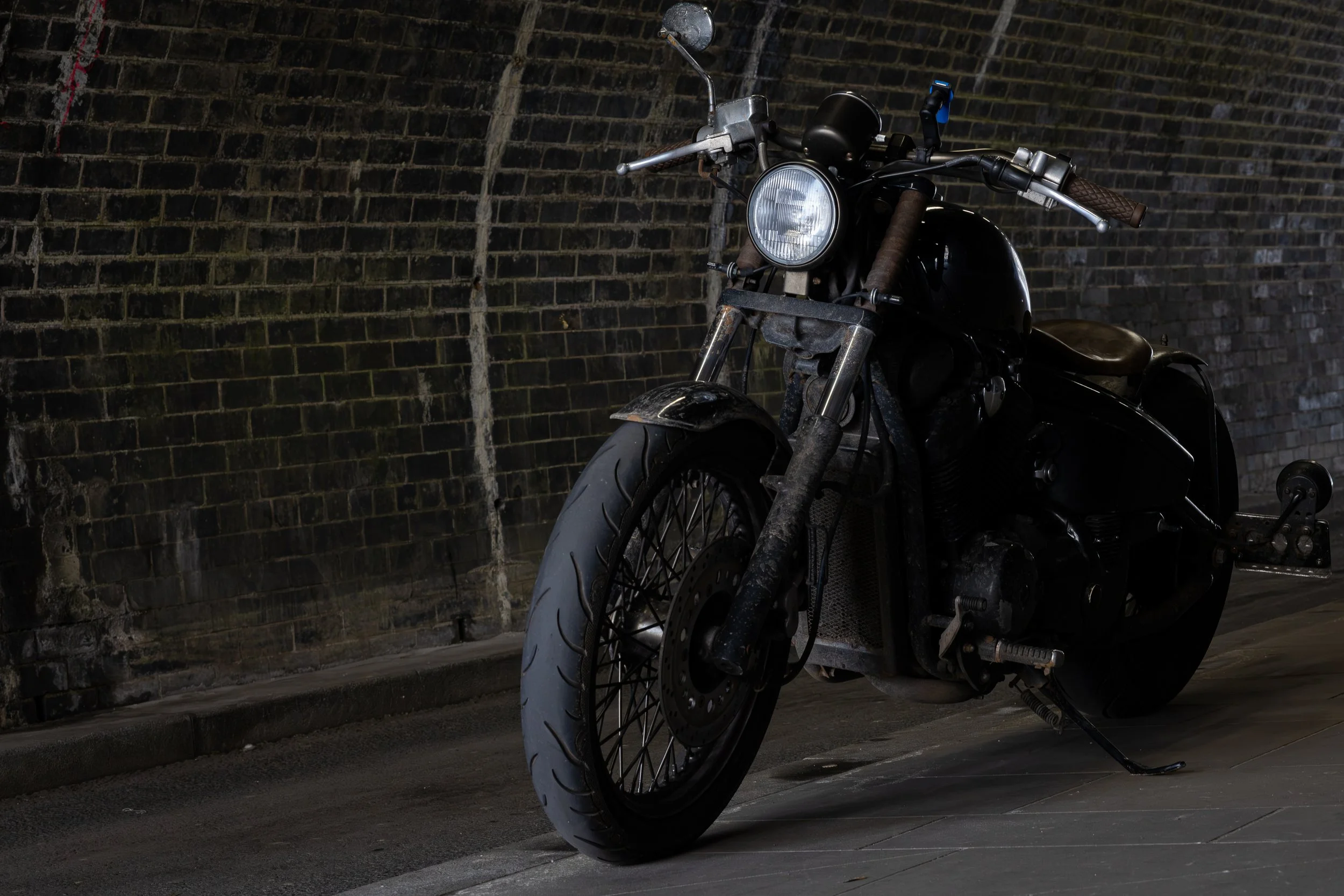 A black motorcycle parked on a street near a brick wall in a tunnel.