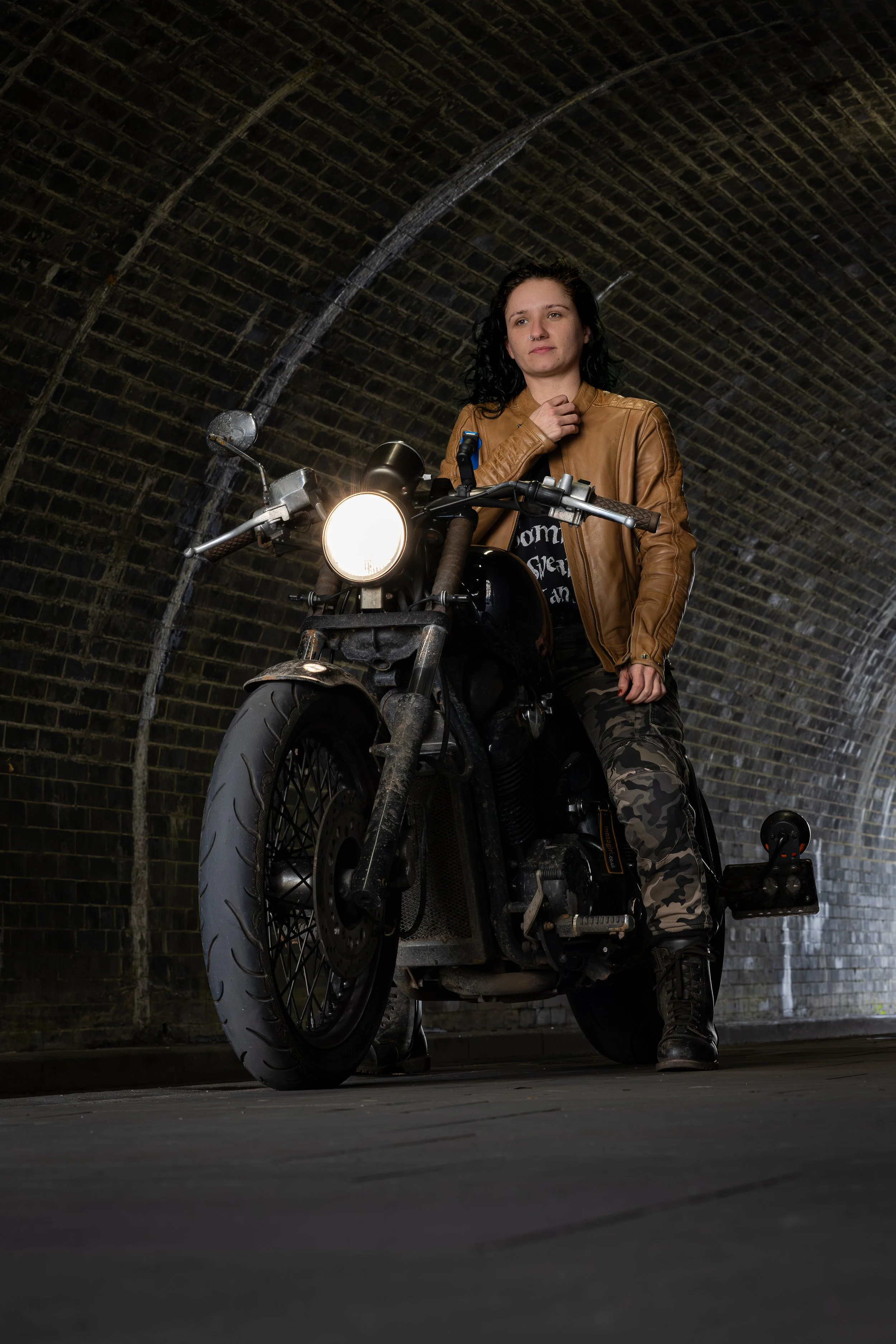 A woman sitting on a black motorcycle inside a brick tunnel.