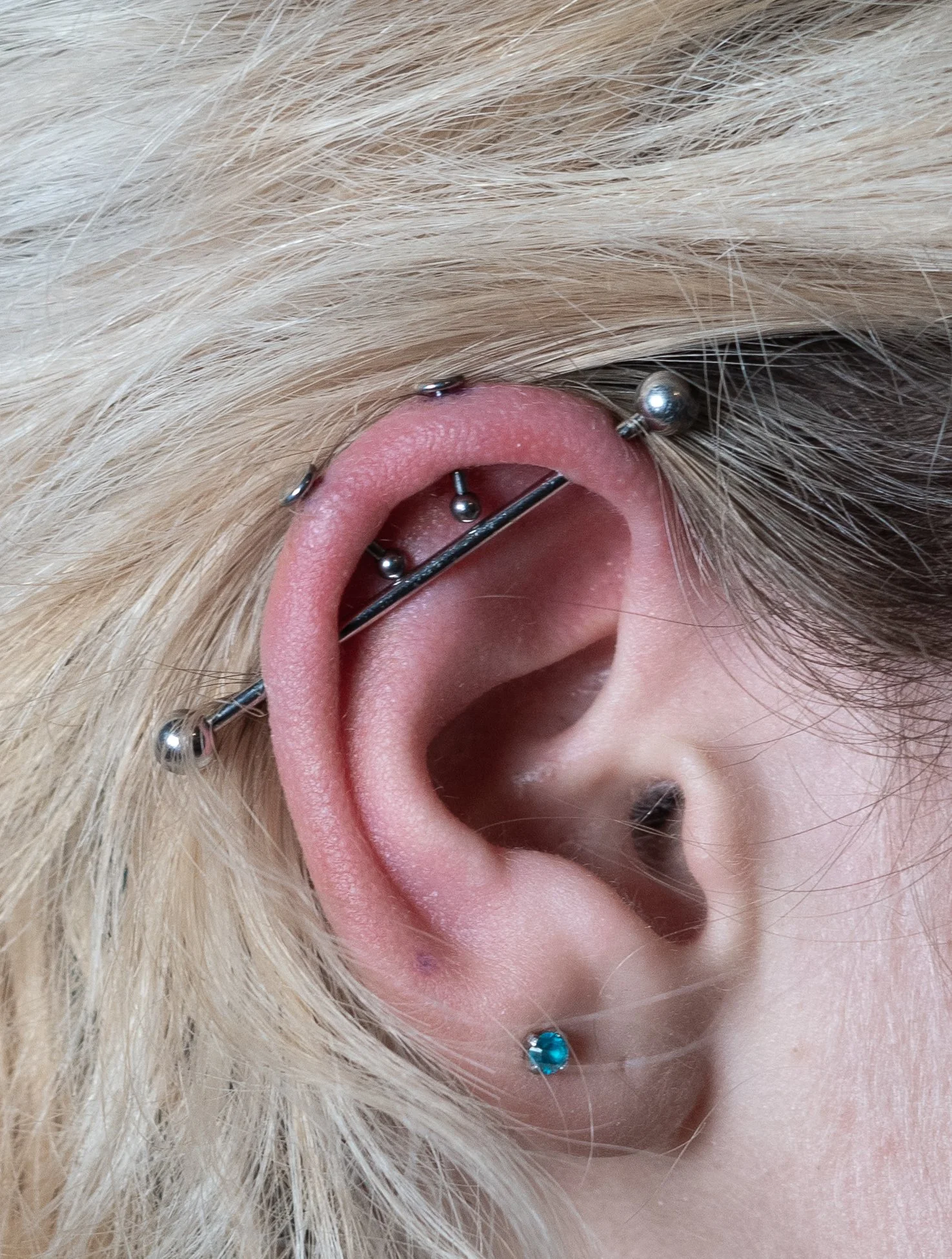 Une oreille humaine avec plusieurs piercings, dont un piercing industriel, eu hélix vertical, une boucle cristalline en bas.