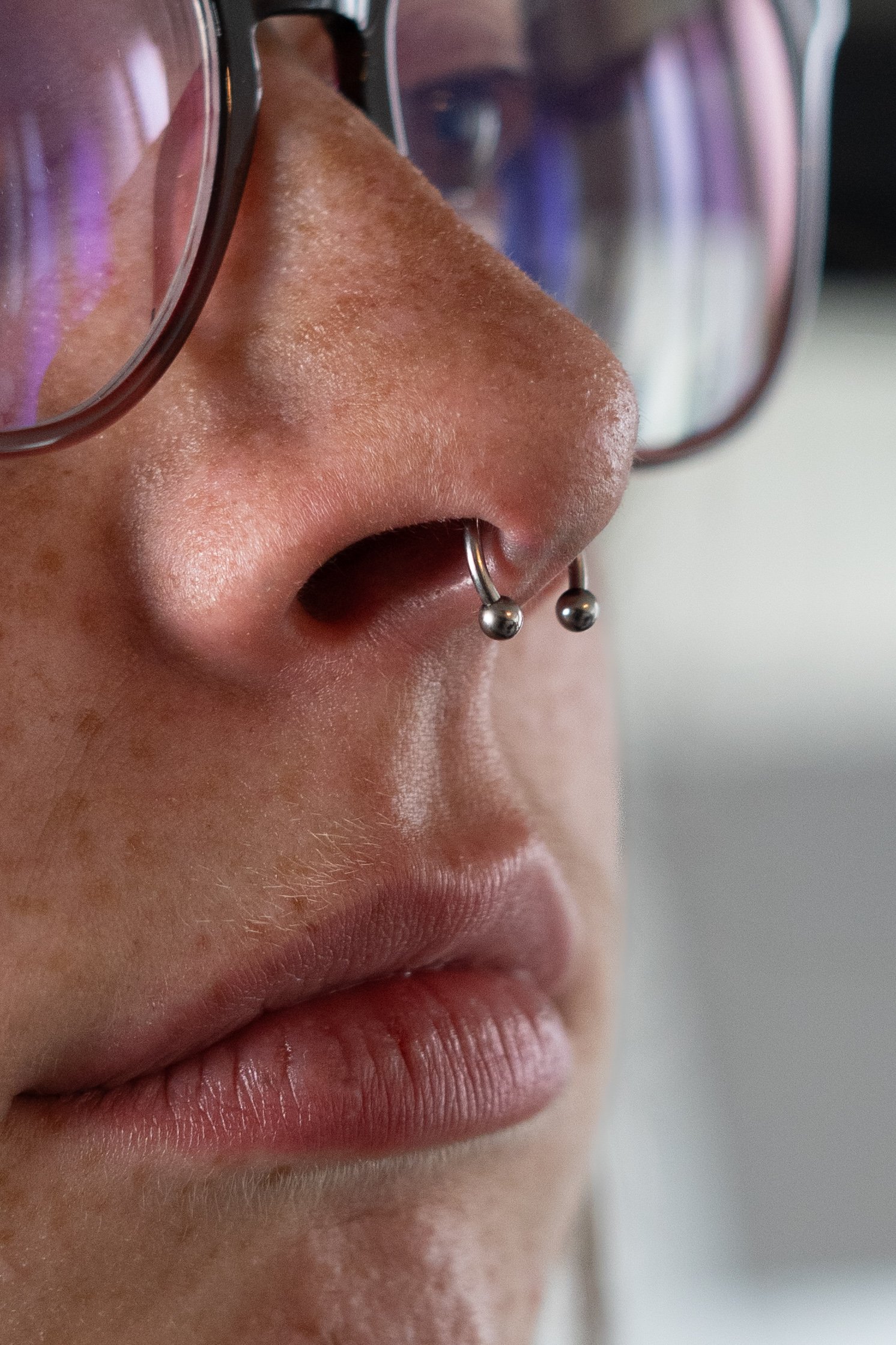 Close-up du visage d'une personne avec lunettes et piercing au nez, montrant les lèvres et le nez.