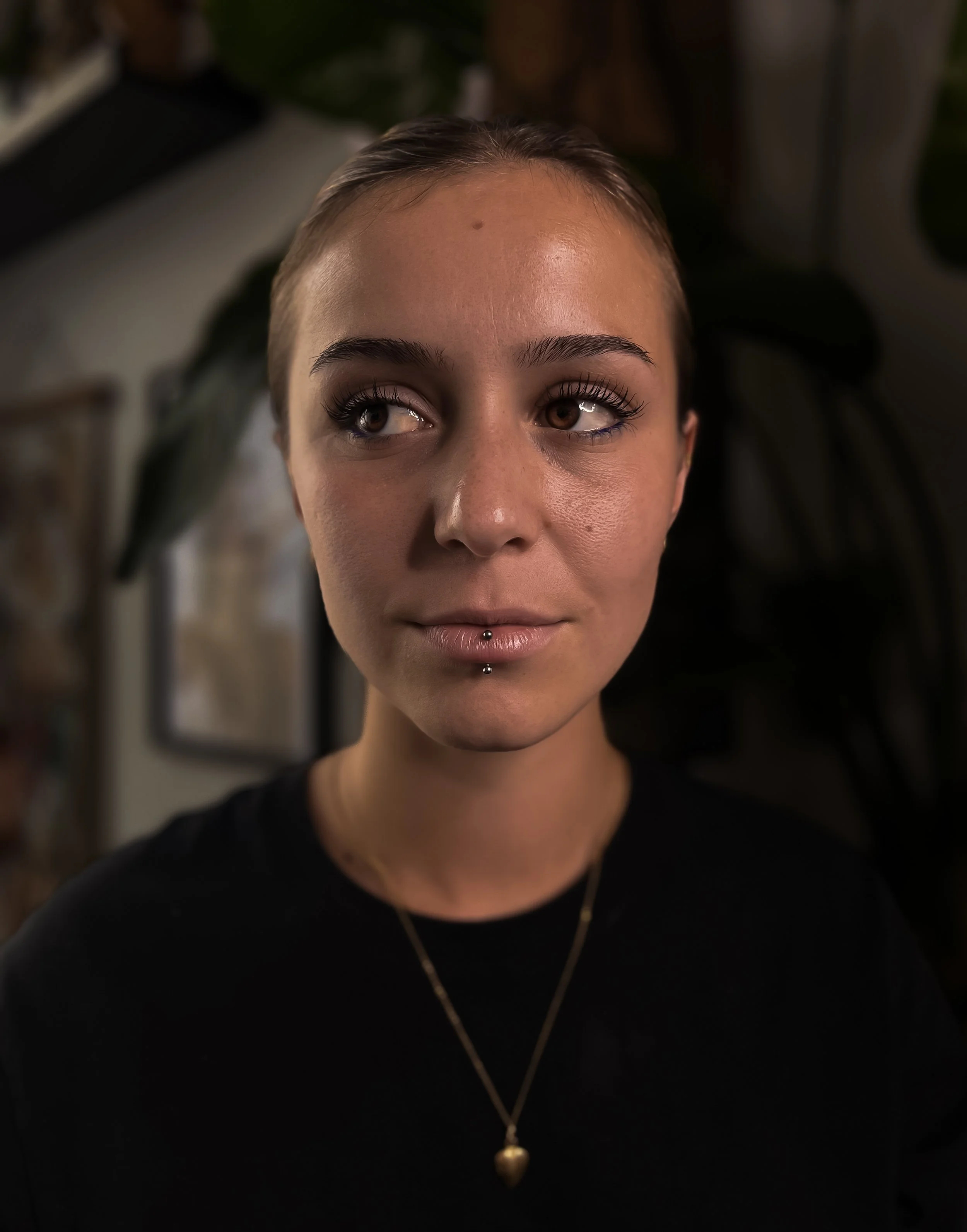 Jeune femme avec piercings au visage, portant un collier en forme de cœur, dans un intérieur