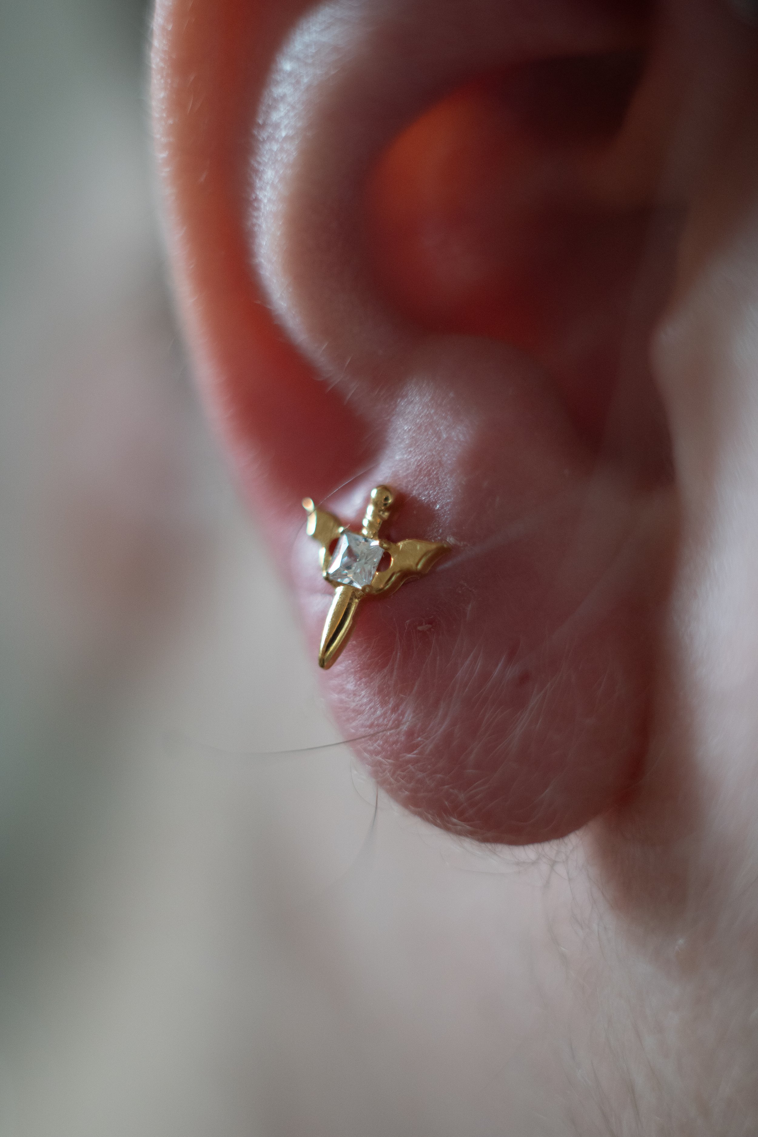 Un piercing à l'oreille avec un bijou en or en forme de petite épée avec un diamant au centre.