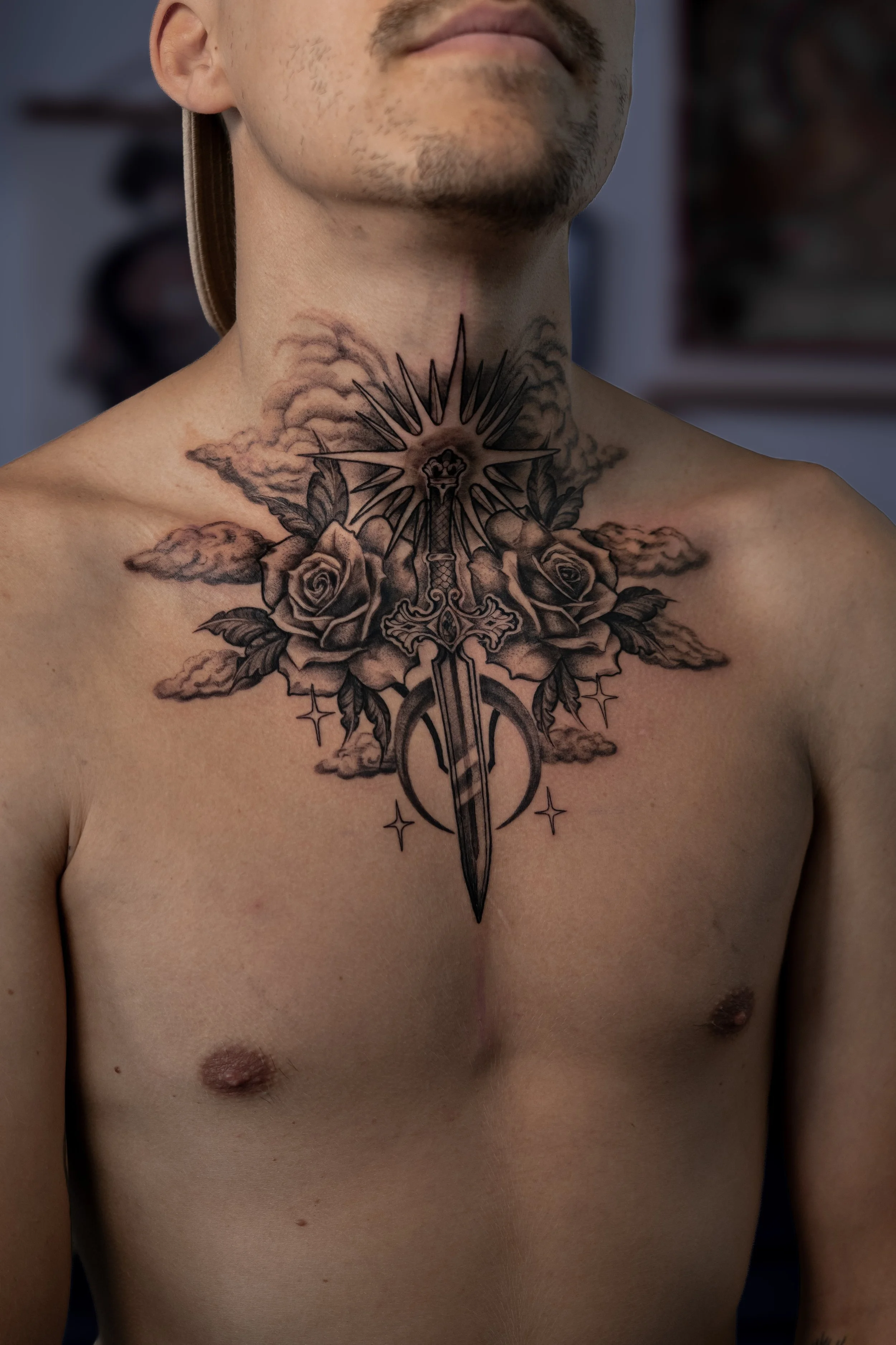 Tatouage sur la poitrine d'un homme représentant une épée, des roses, des nuages et une communion solaire.