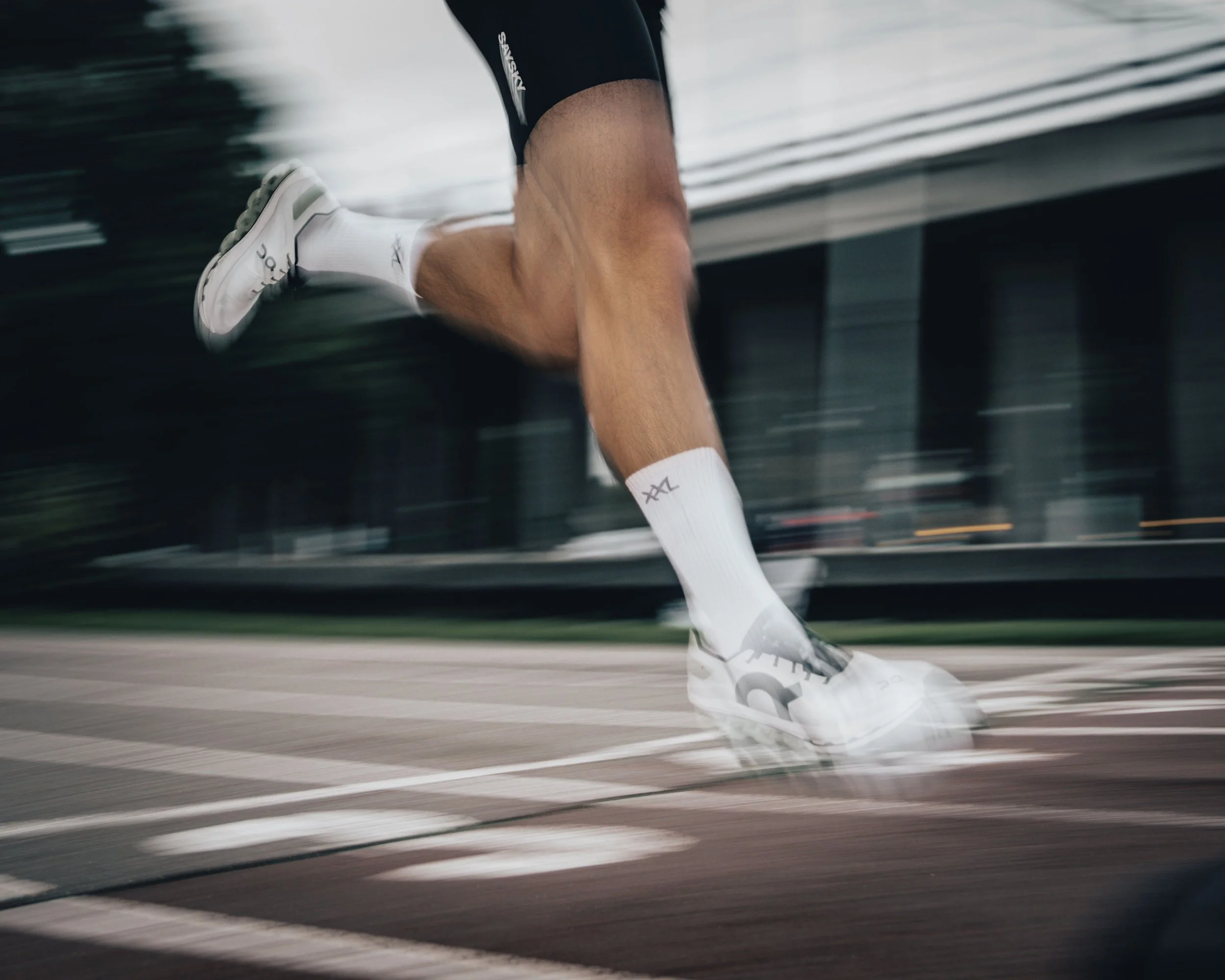 Athlete's legs and feet in white running shoes and white socks running on a track, motion blur indicating speed.