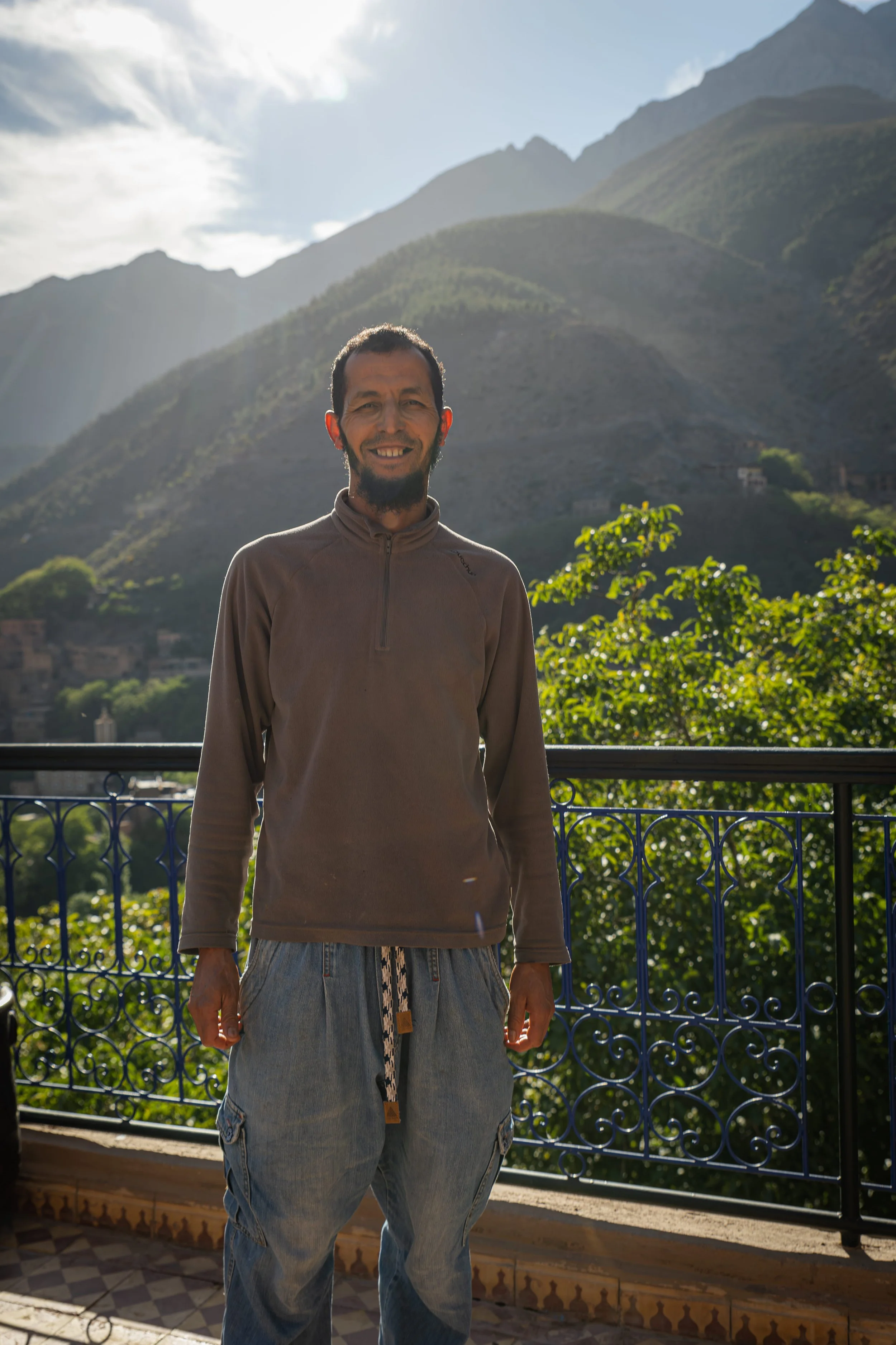 Man standing on balcony with scenic mountainous landscape and greenery in the background.