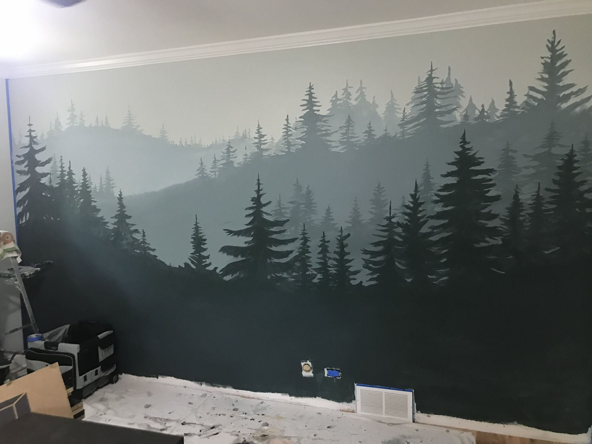 A mural mural of a dense pine forest with layered trees in shades of gray and green, painted on an interior living room wall.