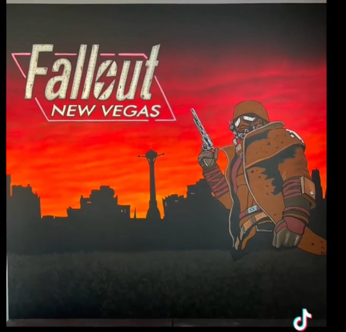 A digital illustration of a character from Fallout, set against a Vegas city skyline at sunset with a red and orange sky. The character is wearing a brown jacket, dark goggles, and holding a gun. The Fallout New Vegas logo is displayed in the top lef