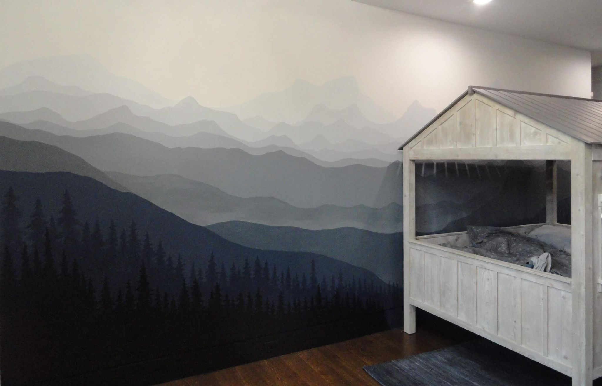 A bedroom with a mountain landscape mural on the wall and a wooden bed frame with a mattress.