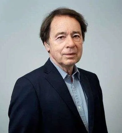 Portrait d'un homme avec des cheveux bruns, portant une veste noire et une chemise bleue claire.