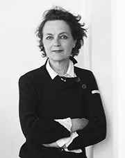 Portrait en noir et blanc d'une femme avec des cheveux bouclés, portant un uniforme noir avec un col blanc, bras croisés.