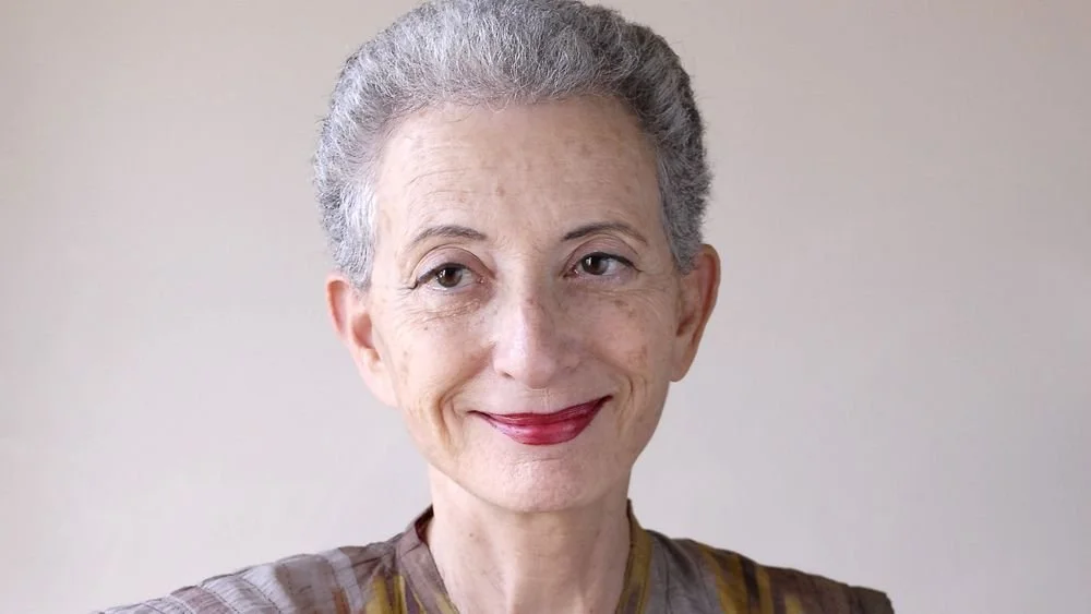 Portrait d'une femme âgée avec des cheveux gris, souriante, portant un vêtement à rayures.