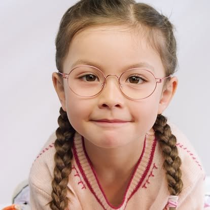 A young girl with glasses and braided hair smiling at the camera.
