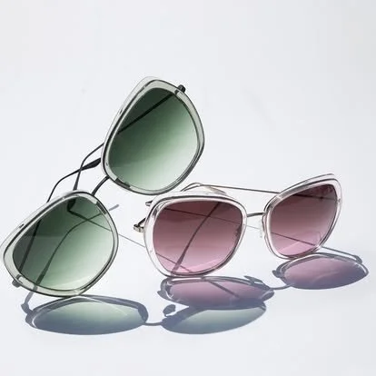 Two pairs of sunglasses, one with green lenses and one with pink lenses, placed on a white surface.