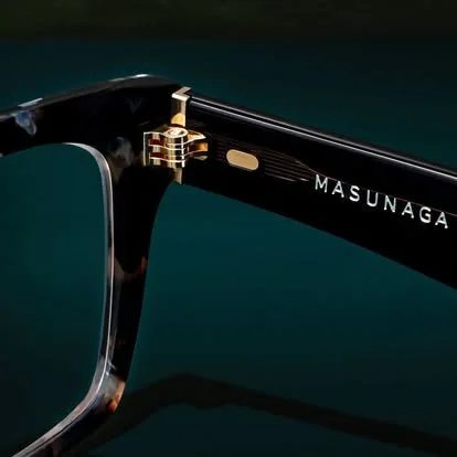 Close-up of black and gold designer eyeglasses with the brand name MasUnaga on the arm.