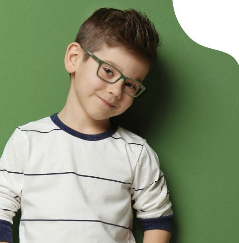 A young boy with short brown hair, green glasses, and a white shirt with navy stripes, smiling and leaning against a green wall.
