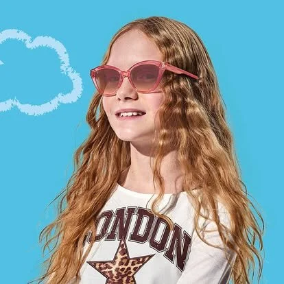 A girl with curly red hair wearing pink sunglasses and a white shirt that says 'LONDON' with a star, standing against a blue background with a cloud illustration.