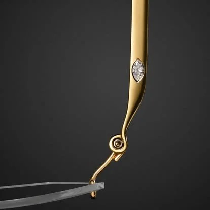 Close-up of a gold jewelry piece with a diamond, attached to a curved metal stand against a dark background.