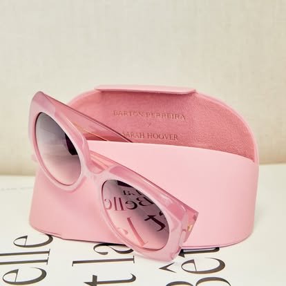 Pink sunglasses with a matching pink case, placed on a surface with partial black text visible.