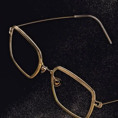 A pair of eyeglasses with a thin metallic frame resting on a black surface with small white specks.