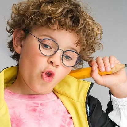 Young boy with curly hair and glasses holding a baseball bat over his shoulder, wearing a yellow jacket and pink shirt.