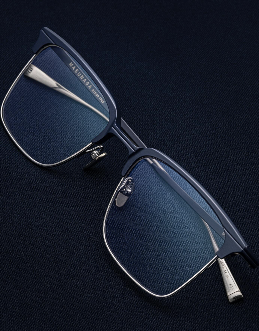 A close-up of stylish rectangular eyeglasses with black frames and silver accents resting on a dark textured surface.