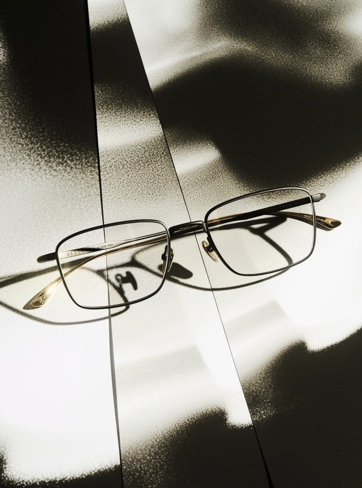 A pair of black-framed eyeglasses resting on a reflective surface, casting a shadow.