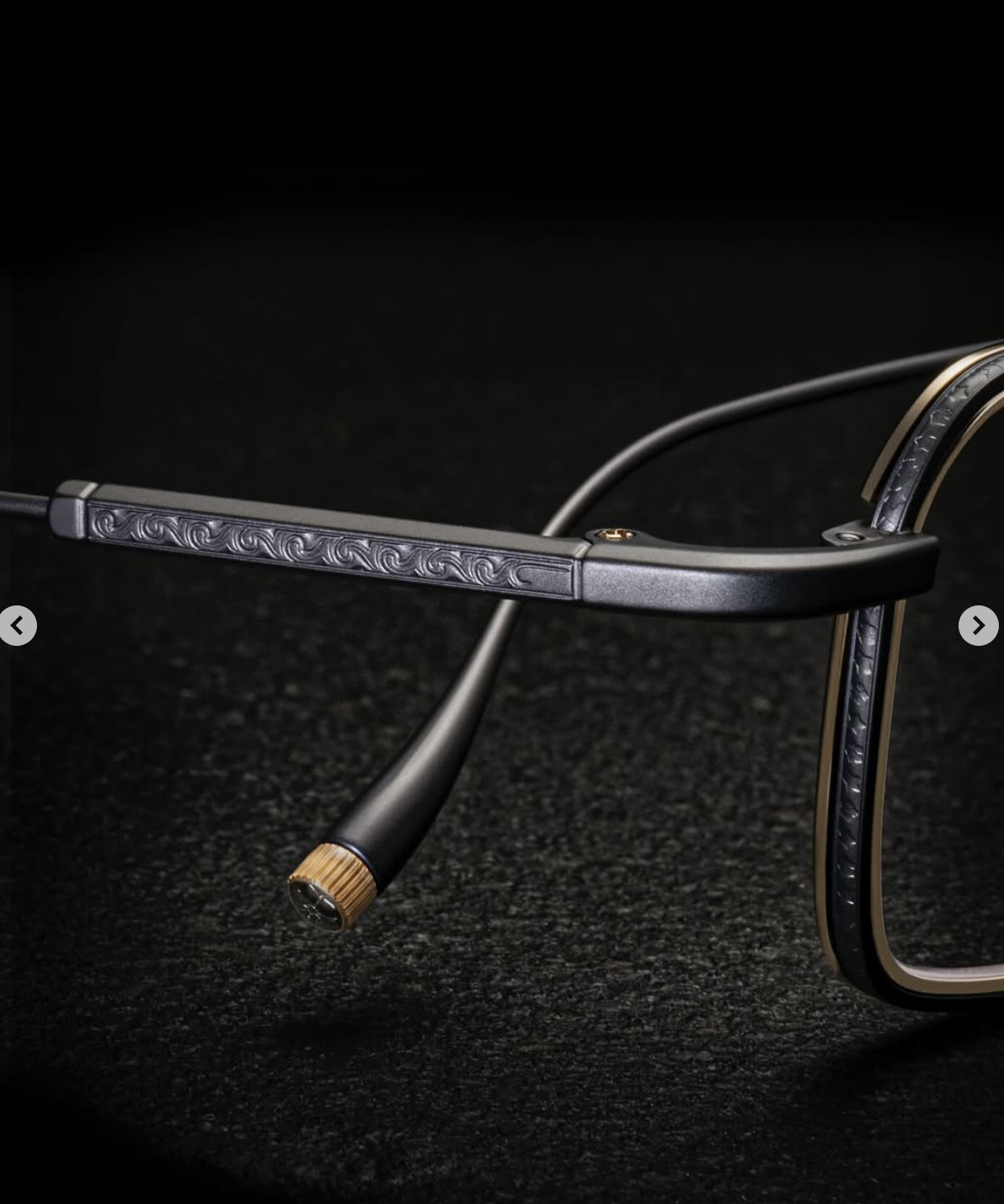 Close-up of sunglasses with intricate engraved details on the black frame, resting on a textured black surface.