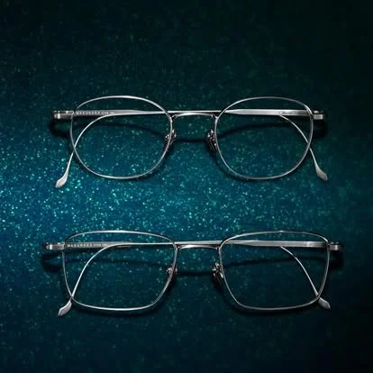 Two pairs of eyeglasses on a sparkly dark green surface.