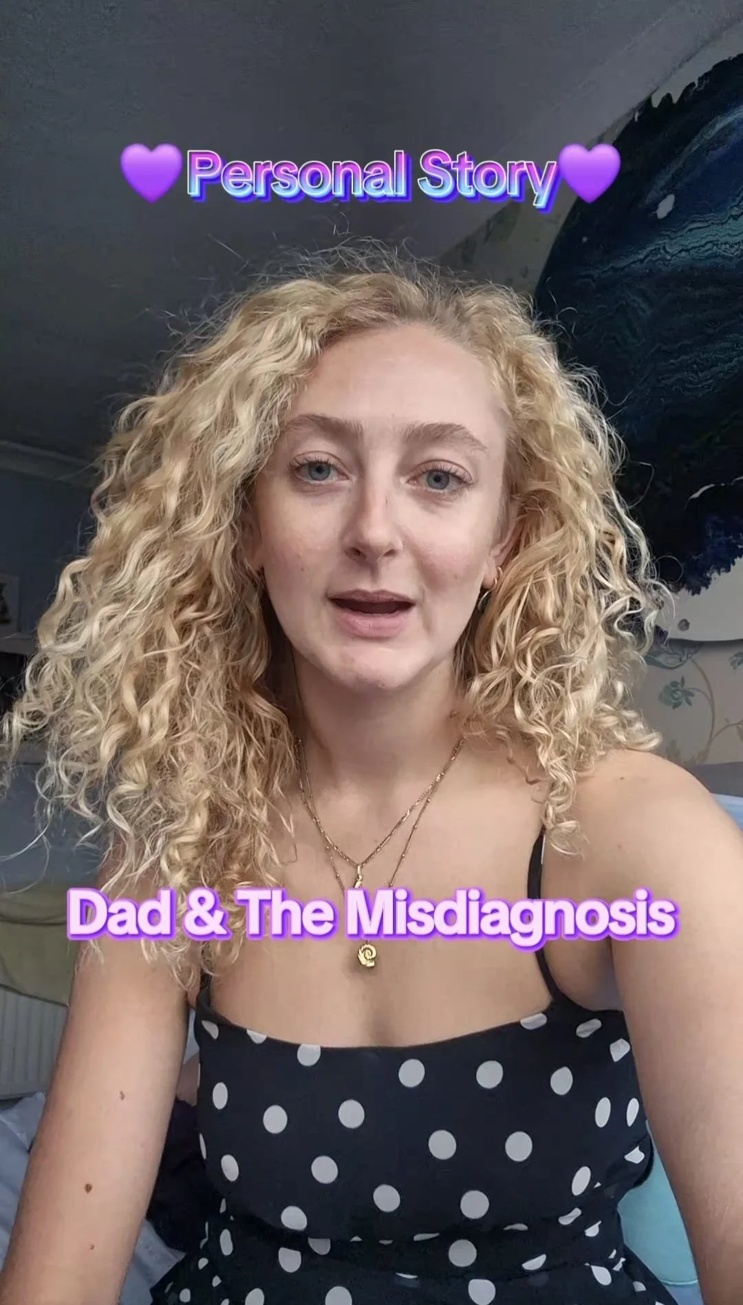 A woman with curly blonde hair and blue eyes takes a selfie in a room. She wears a black polka dot dress and layered necklaces. The photo has text that reads 'Personal Story' with purple hearts and 'Dad & The Misdiagnosis' in purple font.