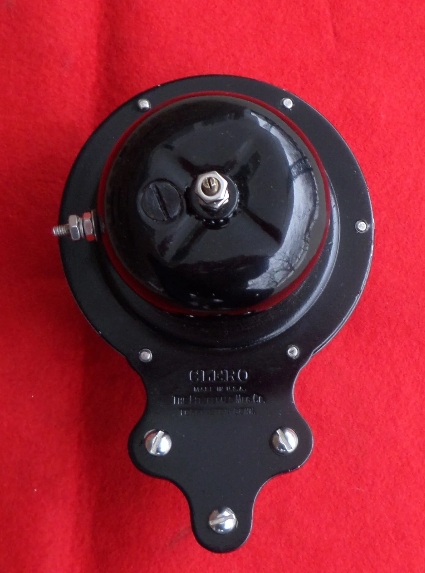 Black mechanical part with a round top mounted on a red background.