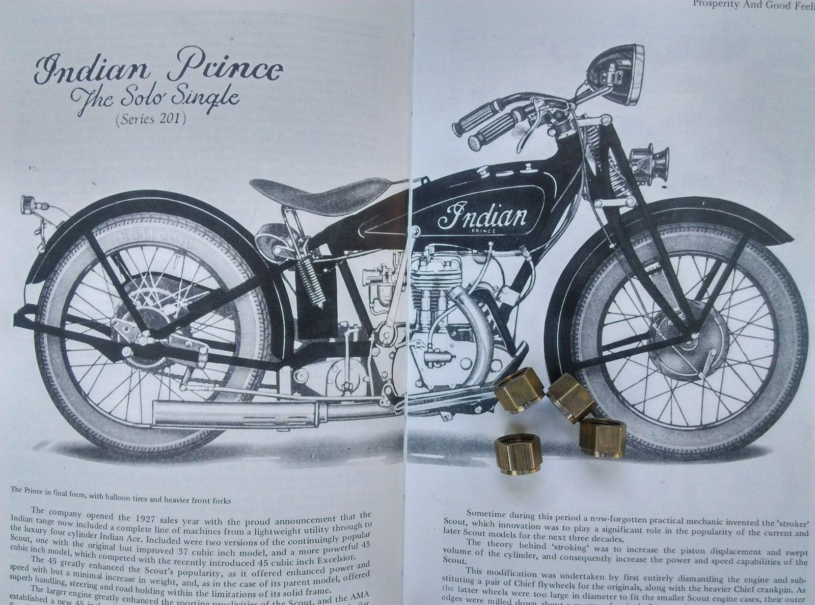 An early 20th-century black and white illustration of an Indian Prince motorcycle, with detailed labeling of its components, including balloon tires and heavier front forks, along with a glass and metal jars placed on the paper.