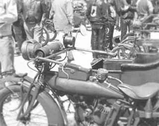 A row of bicycles parked outdoors with people standing nearby, some holding umbrellas.