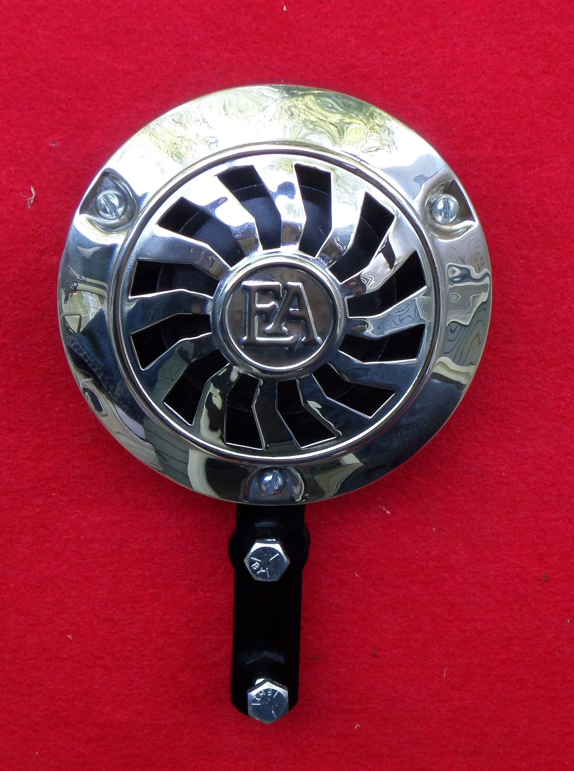 A vintage emergency vehicle siren with a chrome grill and a black mounting bracket against a red background.