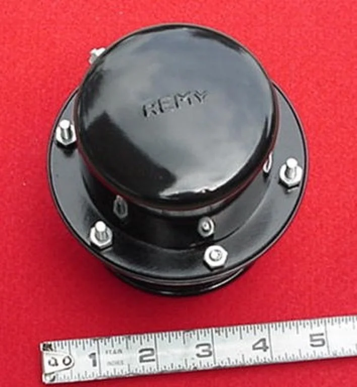 A large black automotive wheel hub with a marked center, placed on a red surface next to a white ruler showing inches for size reference.
