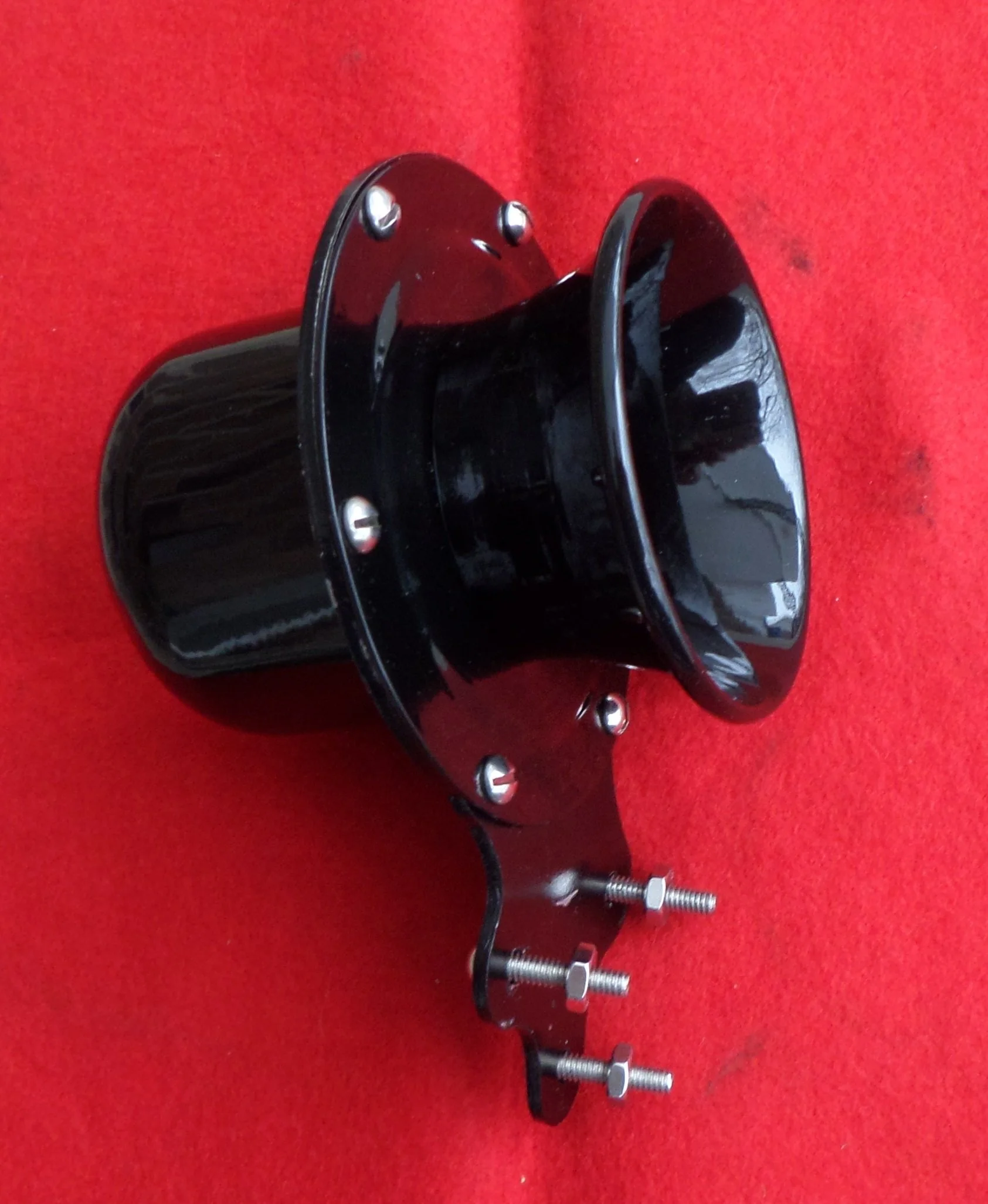 A black directional signal horn with mounting brackets and bolts, set against a red background.